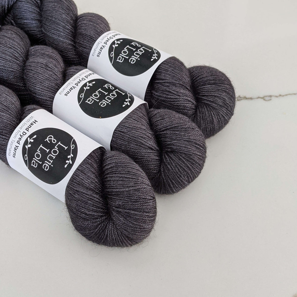Dark gray skeins of yarn with labels on a white surface.