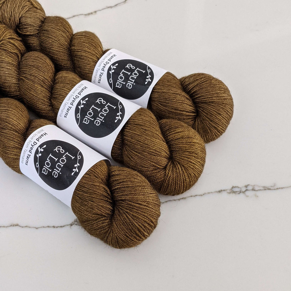 Four skeins of brown yarn on a marble surface with black and white labels.