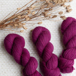 Three skeins of magenta yarn and dried flowers on a textured surface.