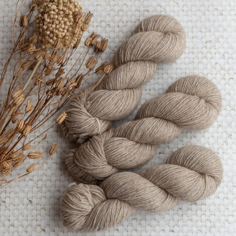 Beige yarn skeins with dried flowers on a textured beige fabric background.