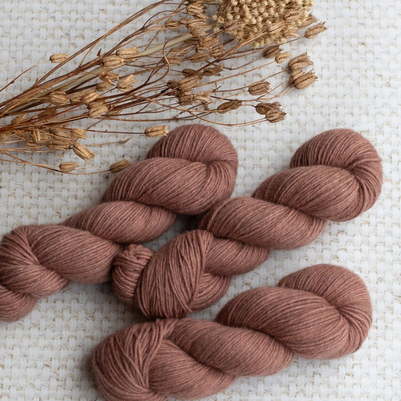Three skeins of brown yarn with dried flowers on a textured surface.