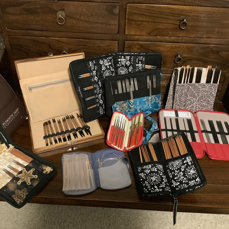 Various sets of knitting needles in colorful cases on a wooden table.