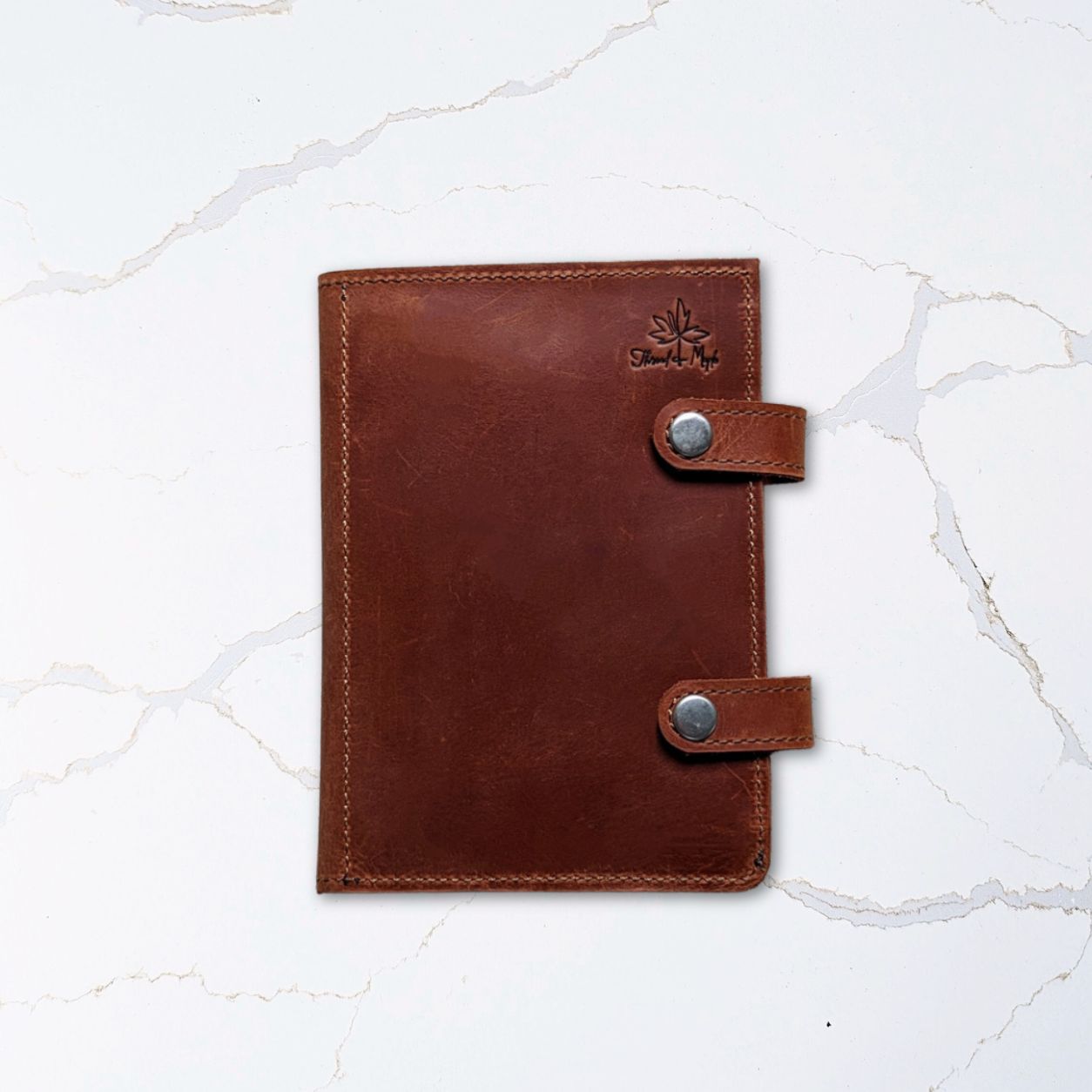 Brown leather journal with button clasps on a white marble surface