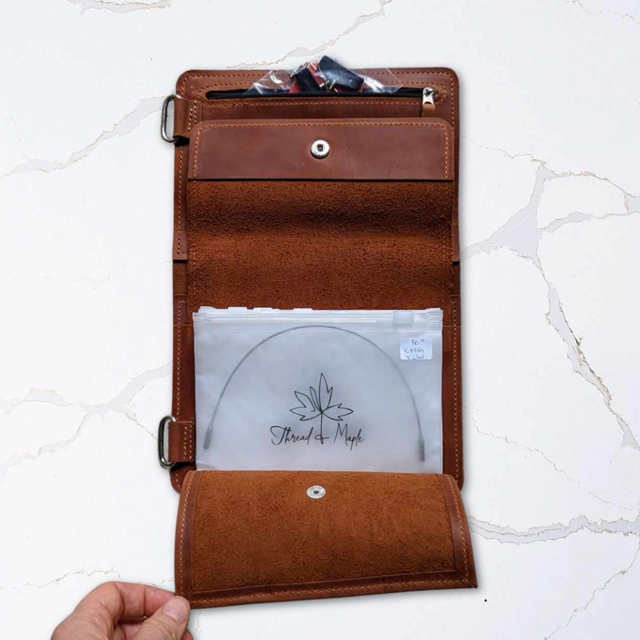 Brown leather document wallet open displaying interior pockets and a transparent file on a marble surface.