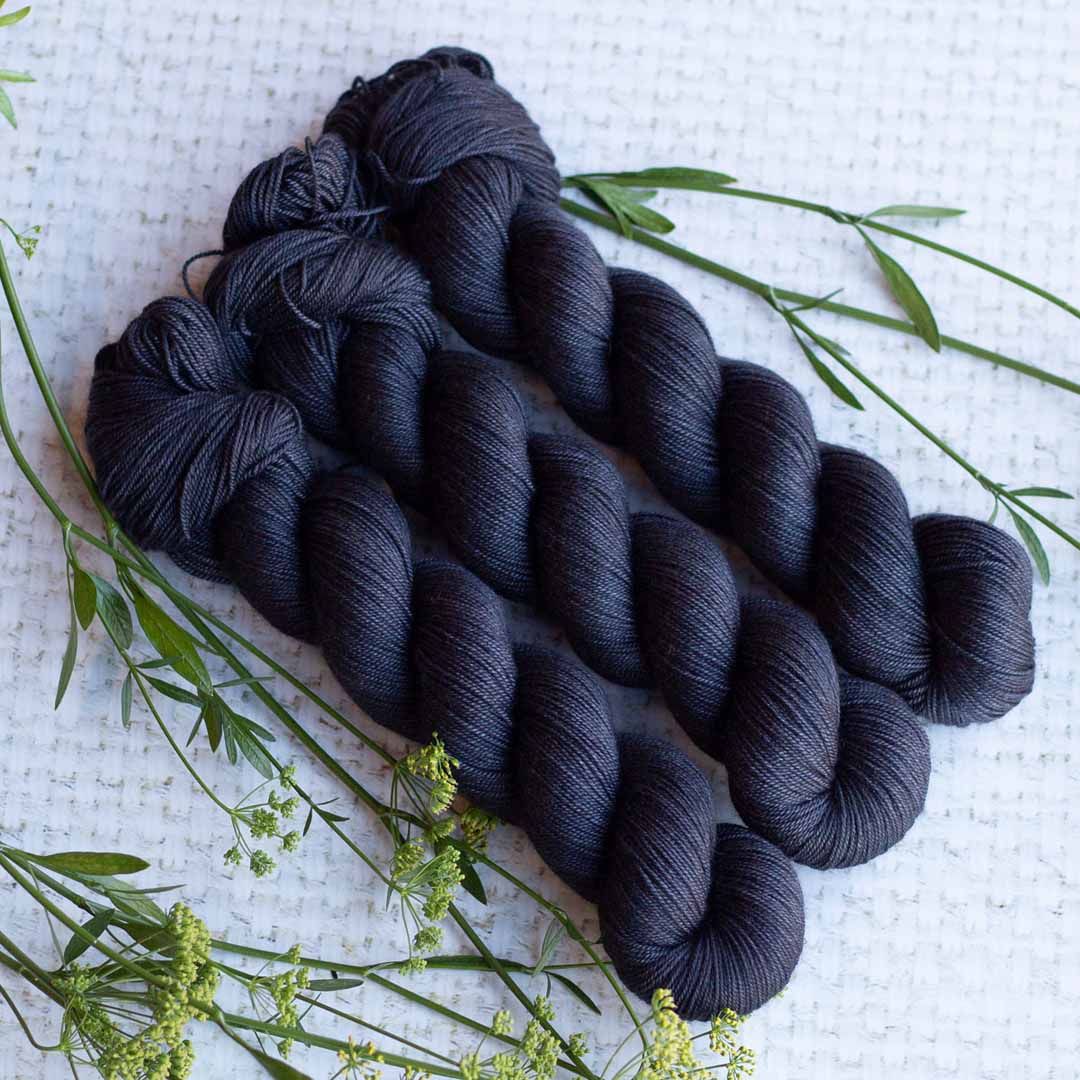Three skeins of dark blue yarn on a textured white surface with sprigs of green foliage.