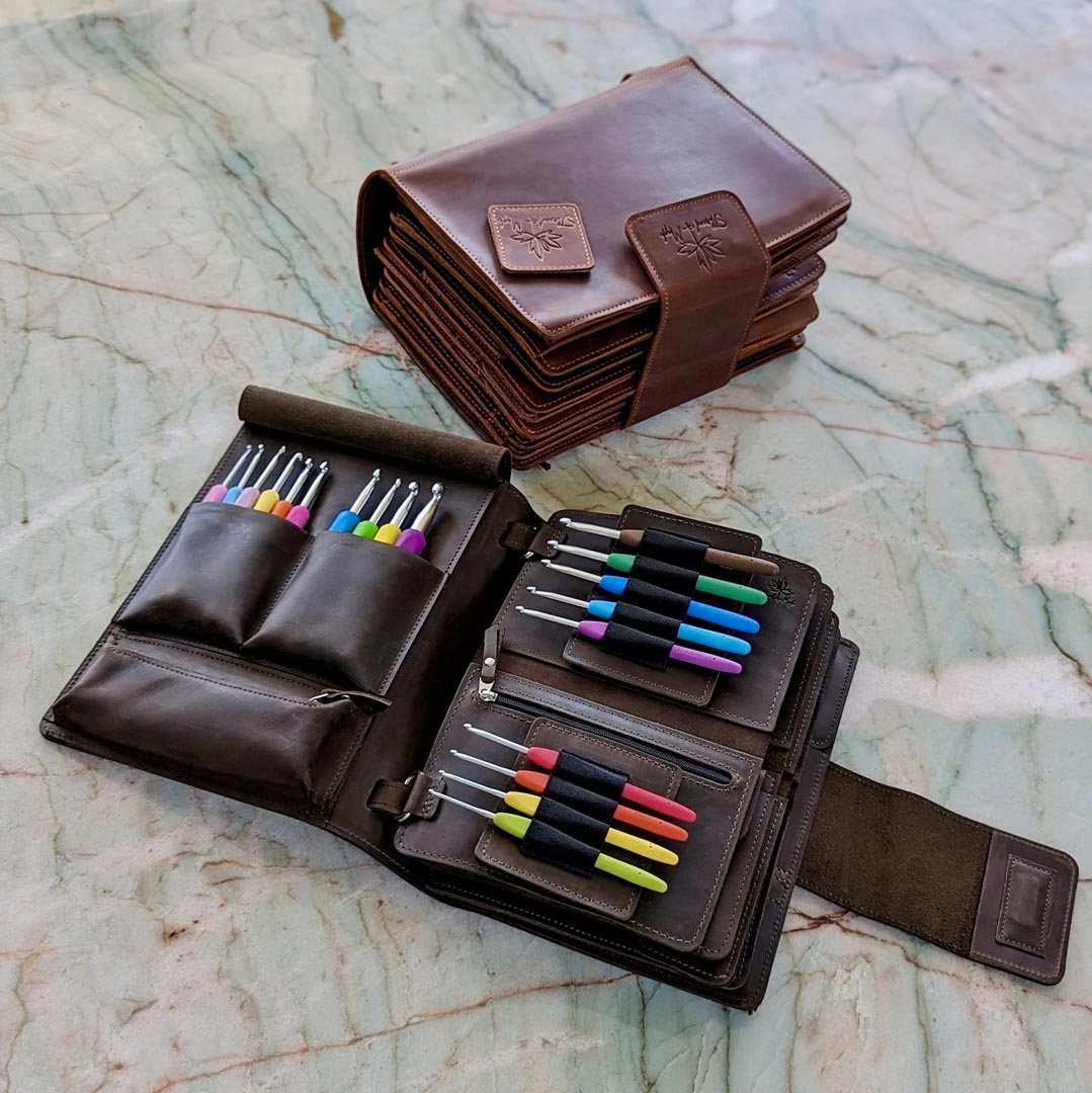 Leather crochet hook case on a marble surface, open to display multiple colorful crochet hooks.