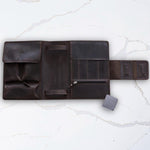 Dark brown leather rolling pouch with compartments on a white marble surface, designed for organizing tools or accessories.