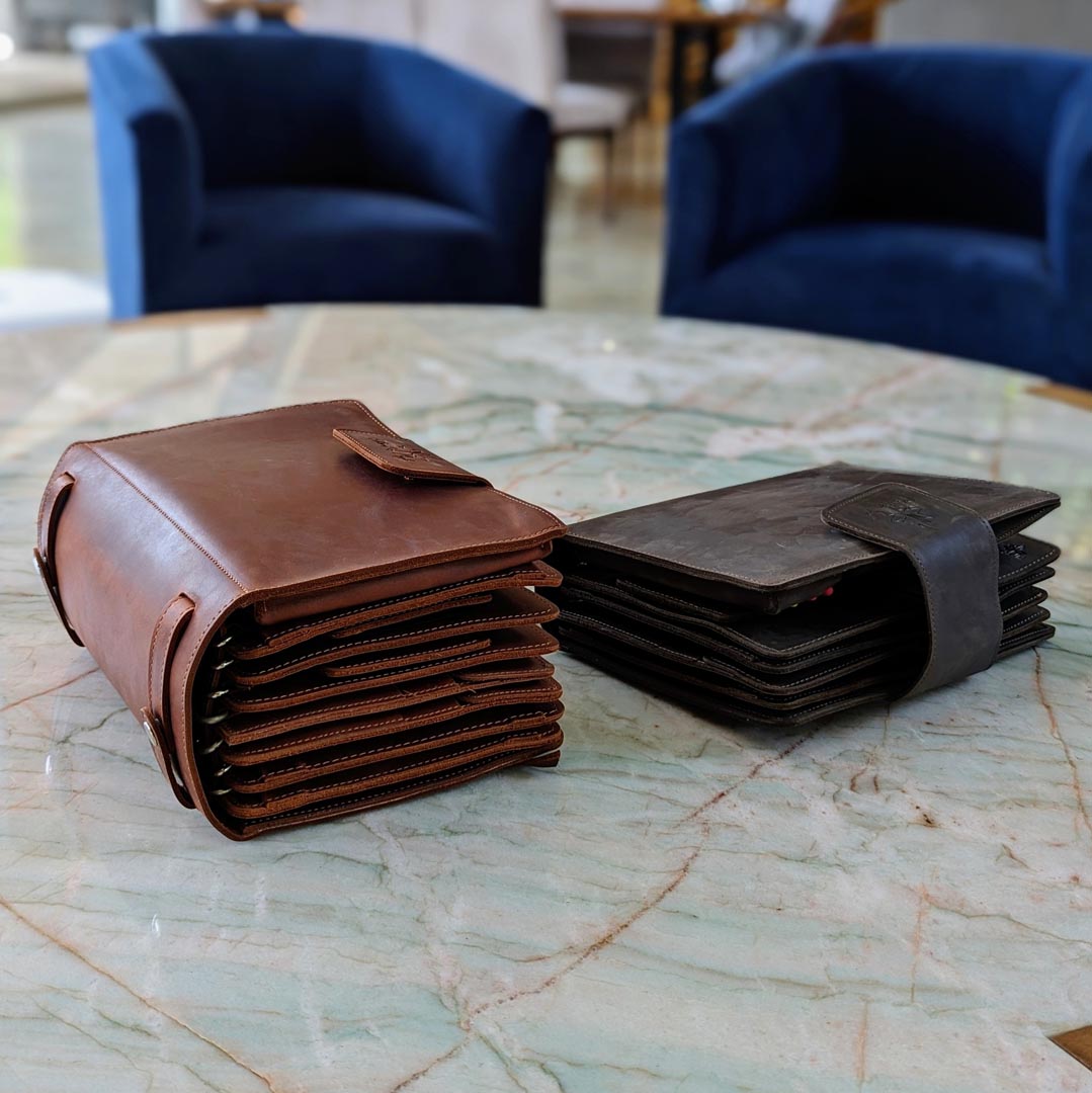 Two leather wallets, one brown and one black, placed on a marble table with blue chairs in the background.