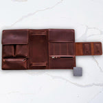 Open brown leather travel organizer on marble surface with multiple compartments and pen holder.