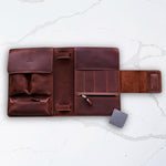 Brown leather travel case with multiple compartments and a magnetic closure, designed for organizing toiletries and accessories, displayed on a white marble surface.