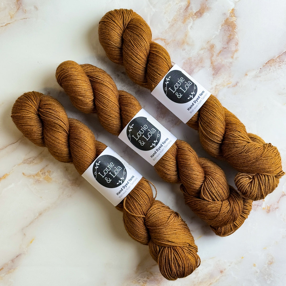 Three skeins of brown yarn on a marble surface with label tags.