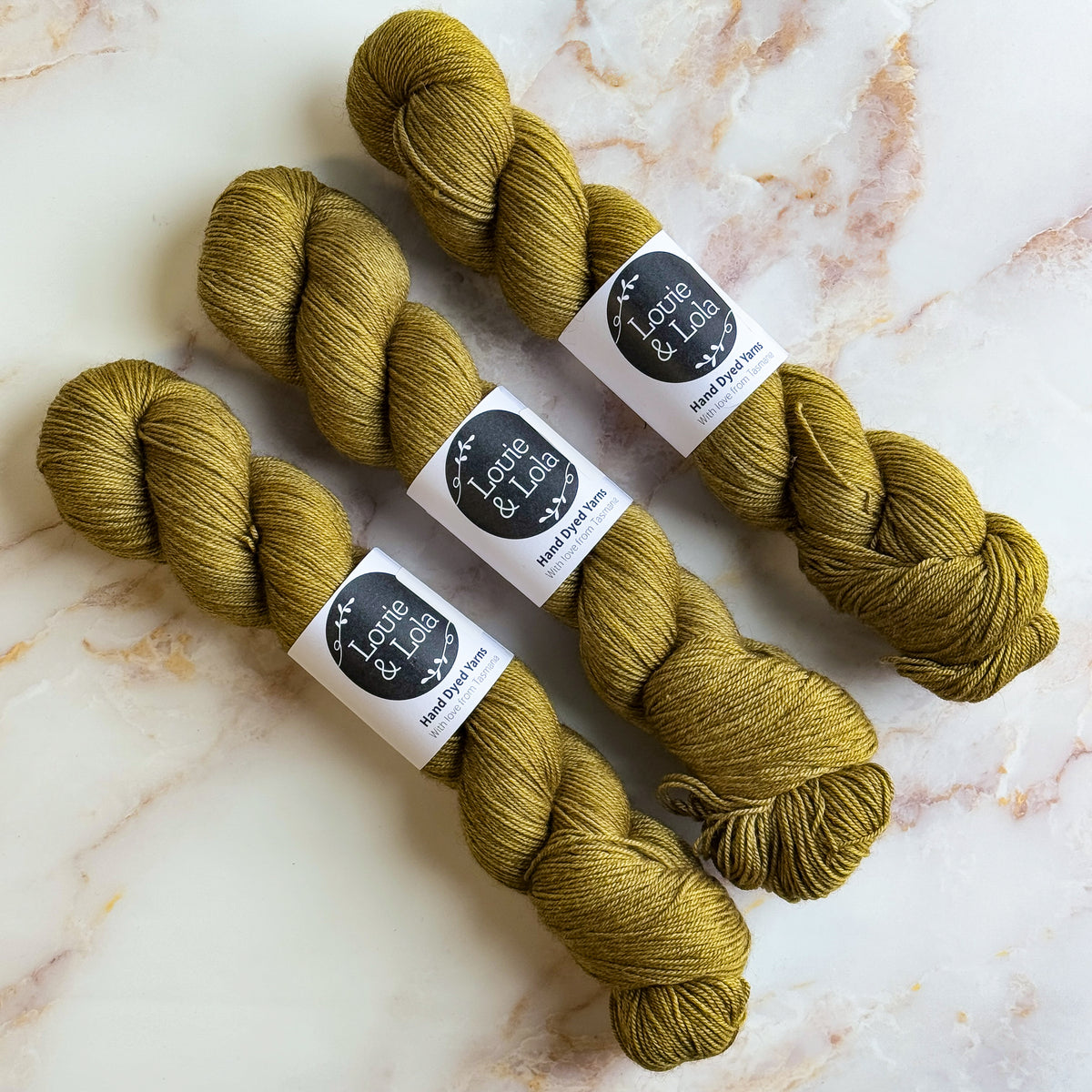 Three skeins of olive green yarn on a marble surface.