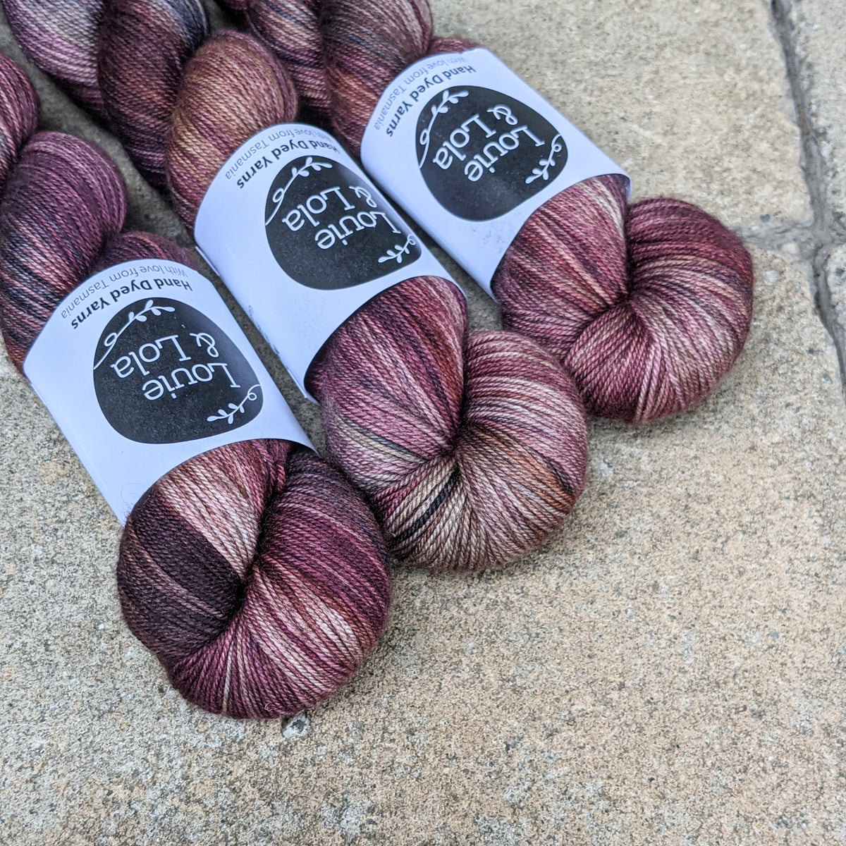 Three skeins of multicolored yarn with labels on a concrete surface.