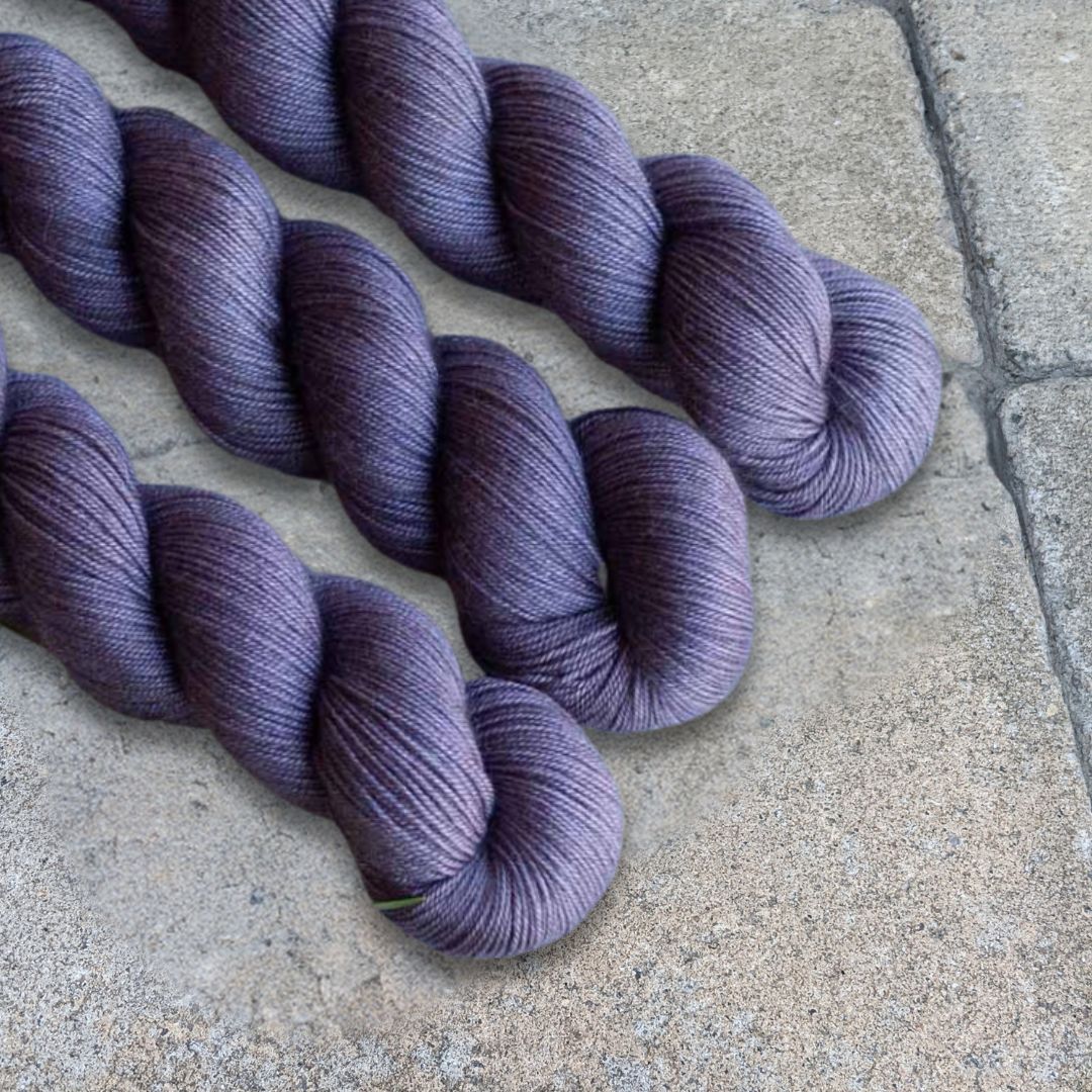 Three skeins of purple yarn on a textured gray surface
