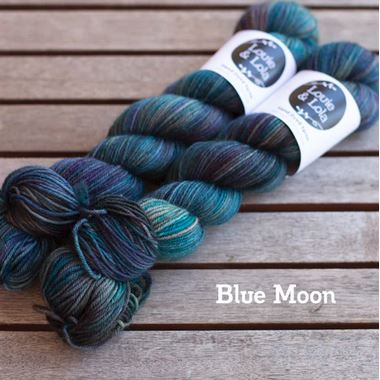 Two skeins of Blue Moon hand-dyed yarn in shades of blue and teal placed on a wooden surface.