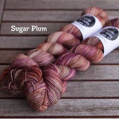 Two skeins of Sugar Plum colored yarn on a wooden table.