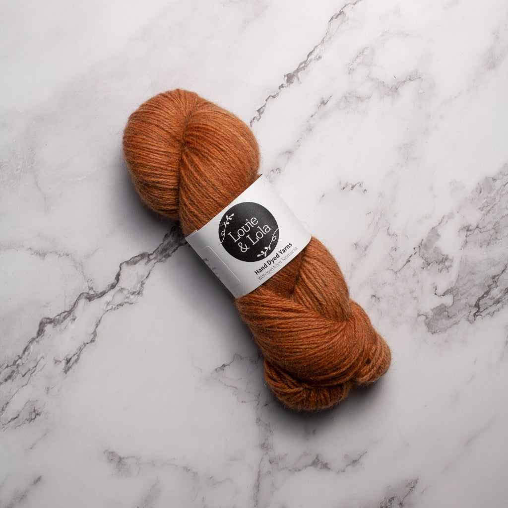 Orange skein of yarn on a marble surface with a branded label.