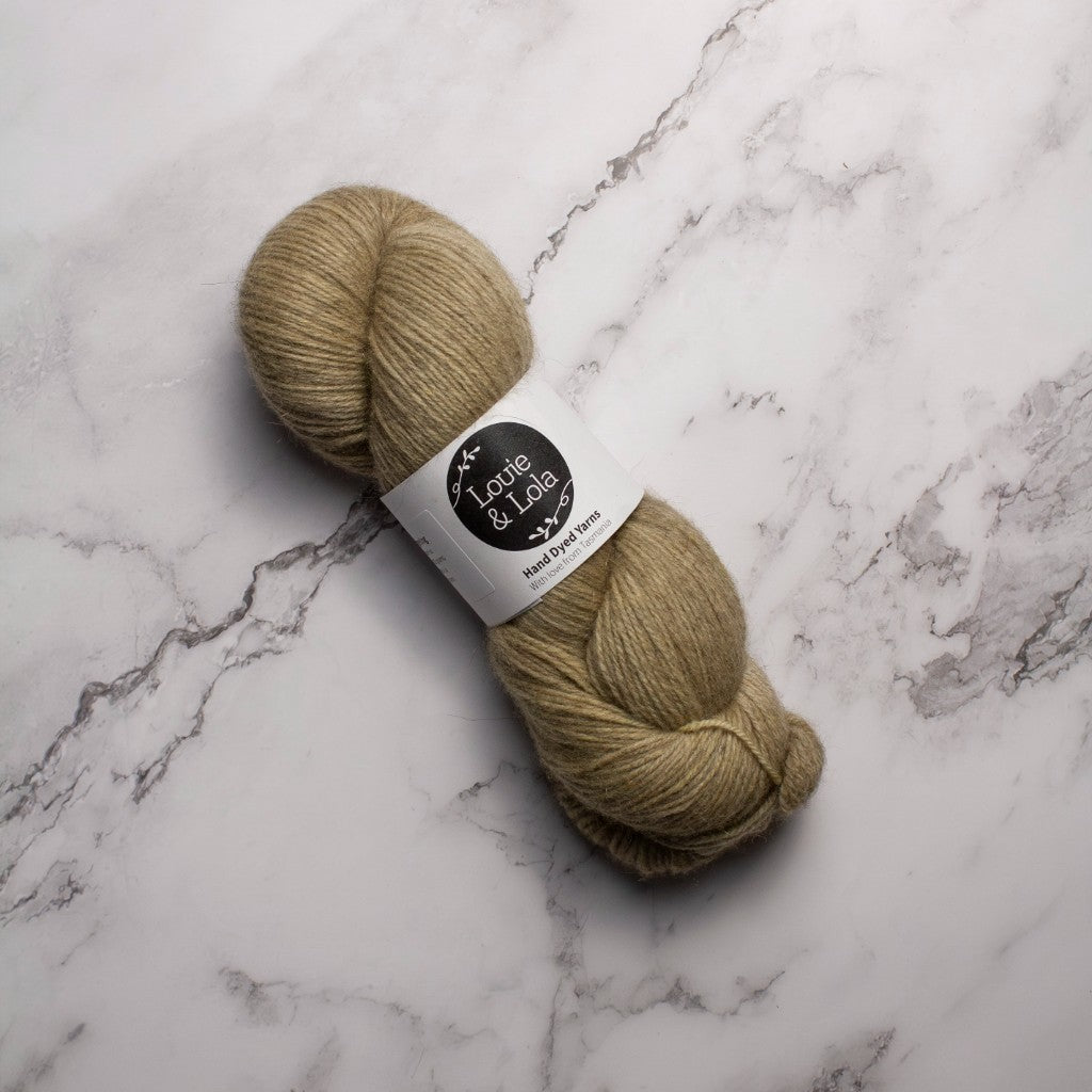 Beige yarn skein labeled Louie & Lola on marble surface.
