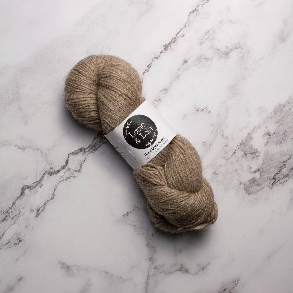 A skein of light brown yarn on a marble surface, labeled with a logo and text.