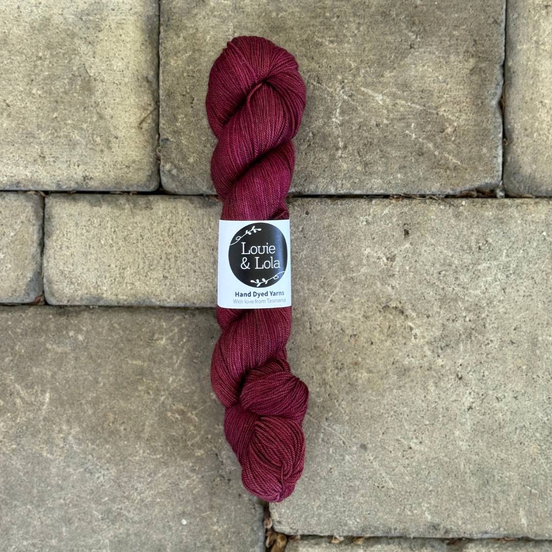 Skein of red yarn on textured stone surface.