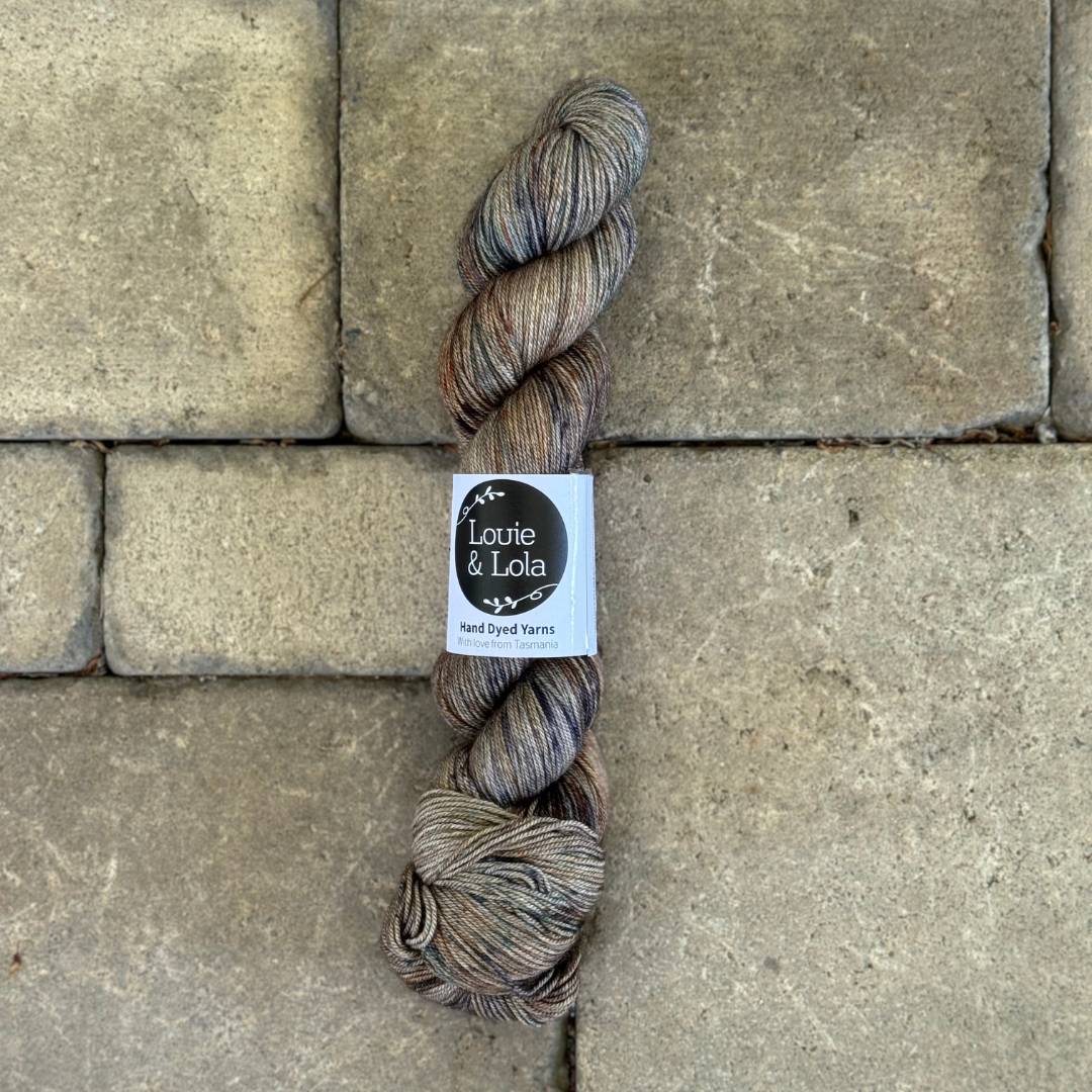 Hand-dyed yarn skein in earthy tones placed on stone pavers