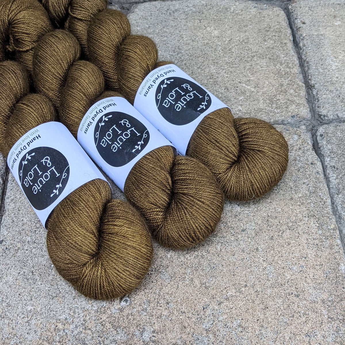 Brown yarn skeins with labels displayed on a stone surface.
