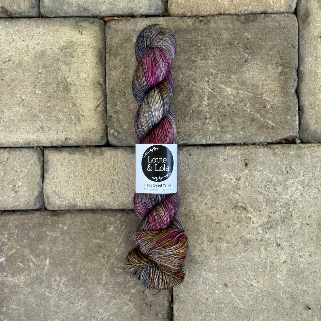 Skein of multicolored yarn with purple, brown, and gray hues on a textured stone background.