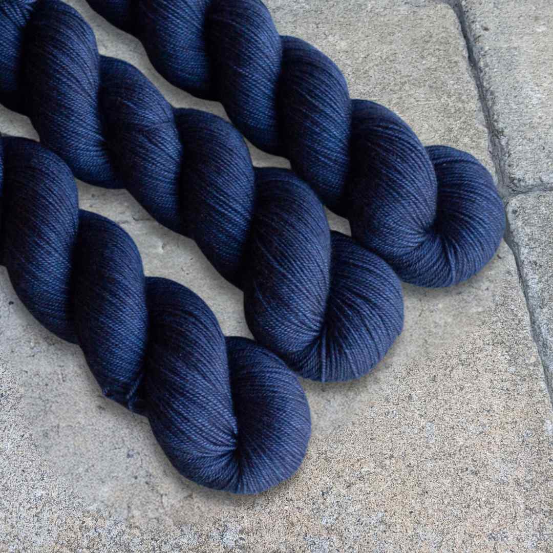 Three skeins of dark blue yarn on a concrete surface.
