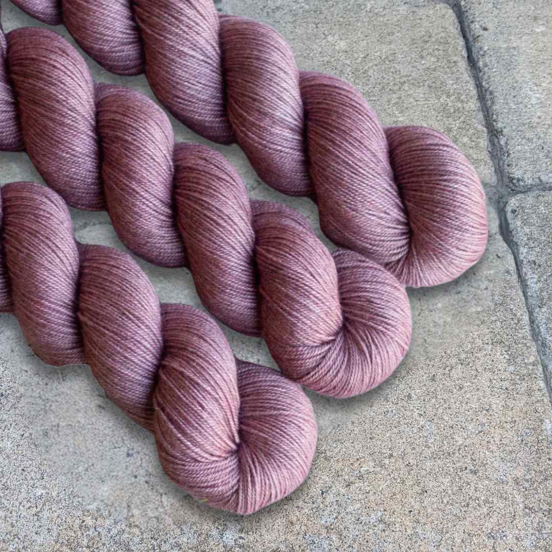 Pinkish-brown skeins of yarn on a tiled floor surface.