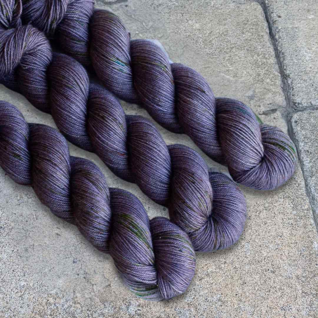 Three skeins of dark purple yarn displayed on a textured stone surface.