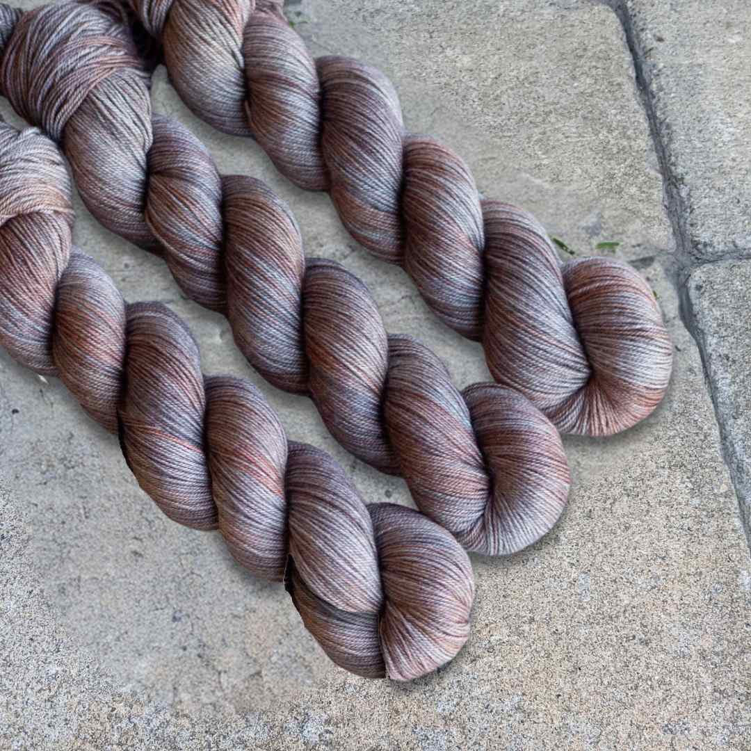 Three skeins of colorful yarn with shades of brown and gray displayed on a textured surface.
