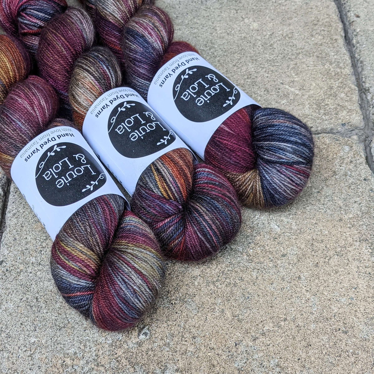 Colorful skeins of yarn on textured stone surface, featuring rich, multicolored hues with labels.