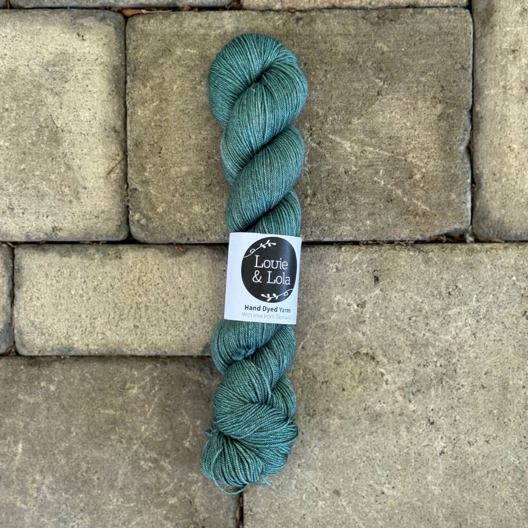 Teal hand-dyed Louie & Lola yarn skein on stone background