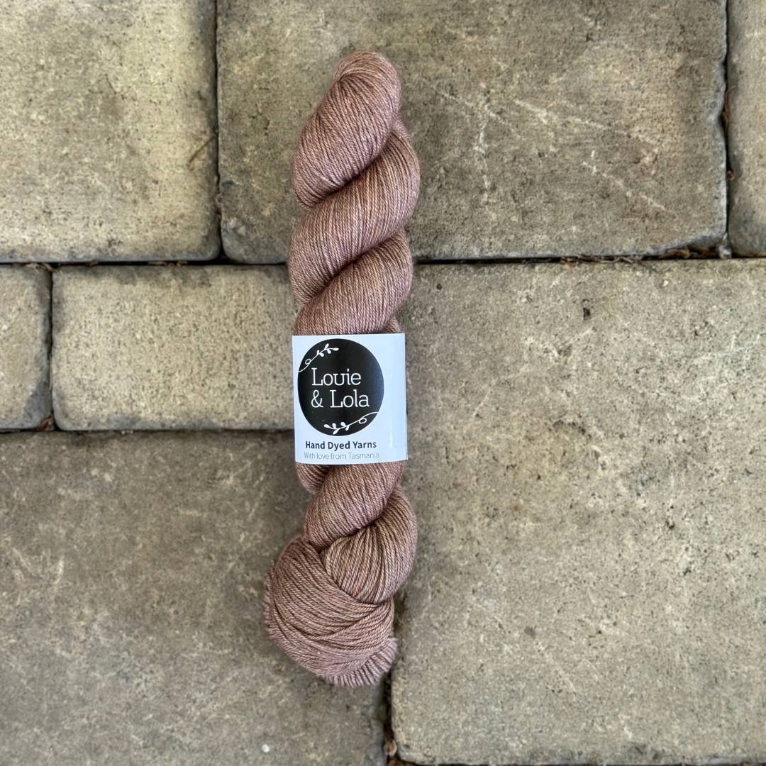 A skein of Louie & Lola hand-dyed yarn in a neutral beige color on a stone tile background.