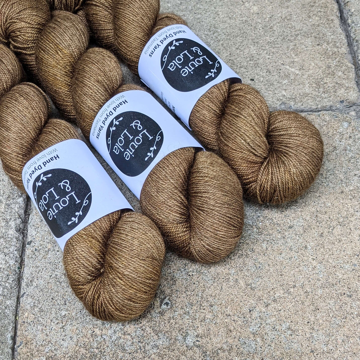 Three skeins of brown yarn labeled for sale on a textured stone surface.
