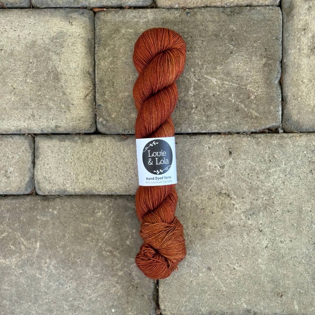 Hand-dyed orange yarn skein on stone background with a Louie & Lola label.