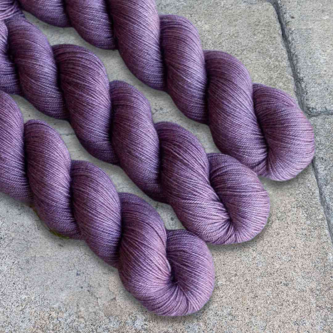 Three skeins of purple yarn arranged on a textured surface.
