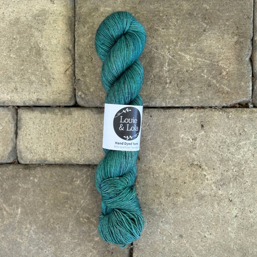 A skein of teal-colored yarn on a textured stone background.