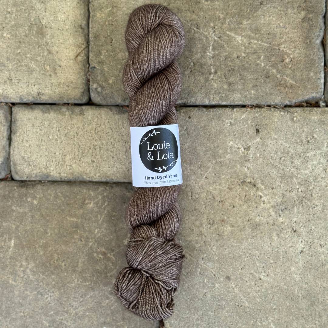 Brown skein of Louie & Lola hand-dyed yarn on a stone surface.