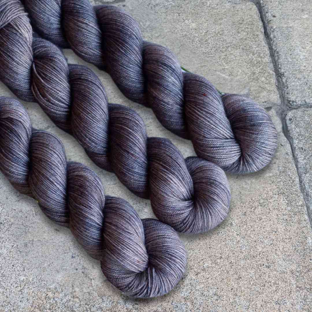 Three skeins of gray yarn on a textured stone background.