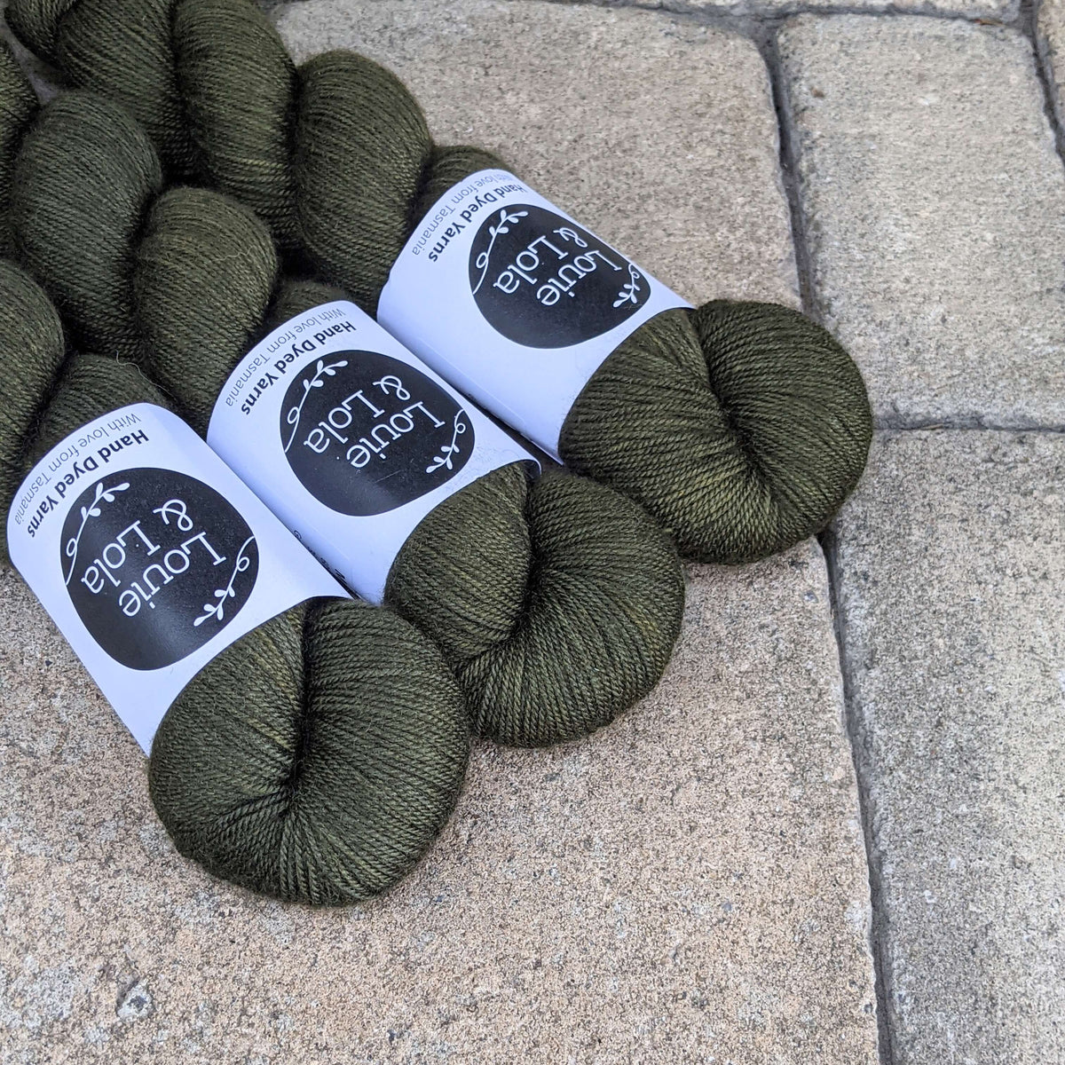 Skeins of dark green yarn with labels on stone pavement background.