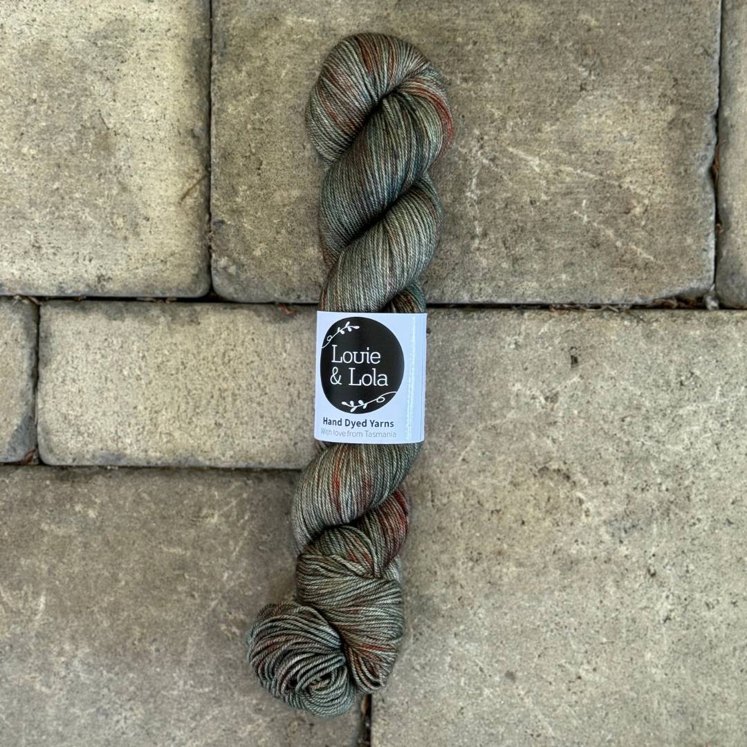 Hand-dyed yarn skein in earthy tones on stone pavement background