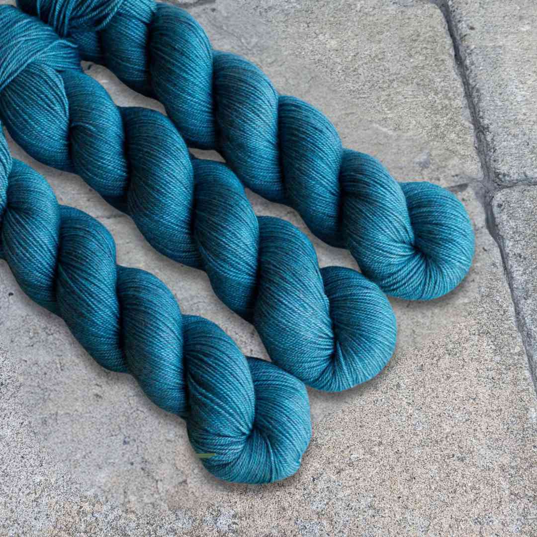 Three skeins of teal-colored yarn displayed on a concrete surface.