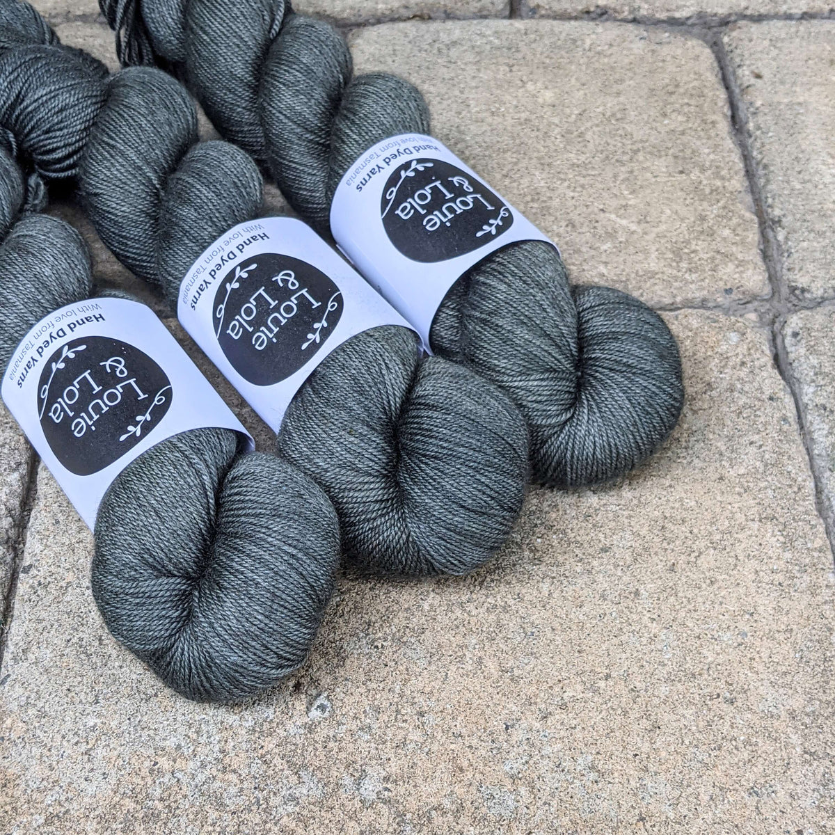 Three skeins of dark gray yarn on a textured stone surface.