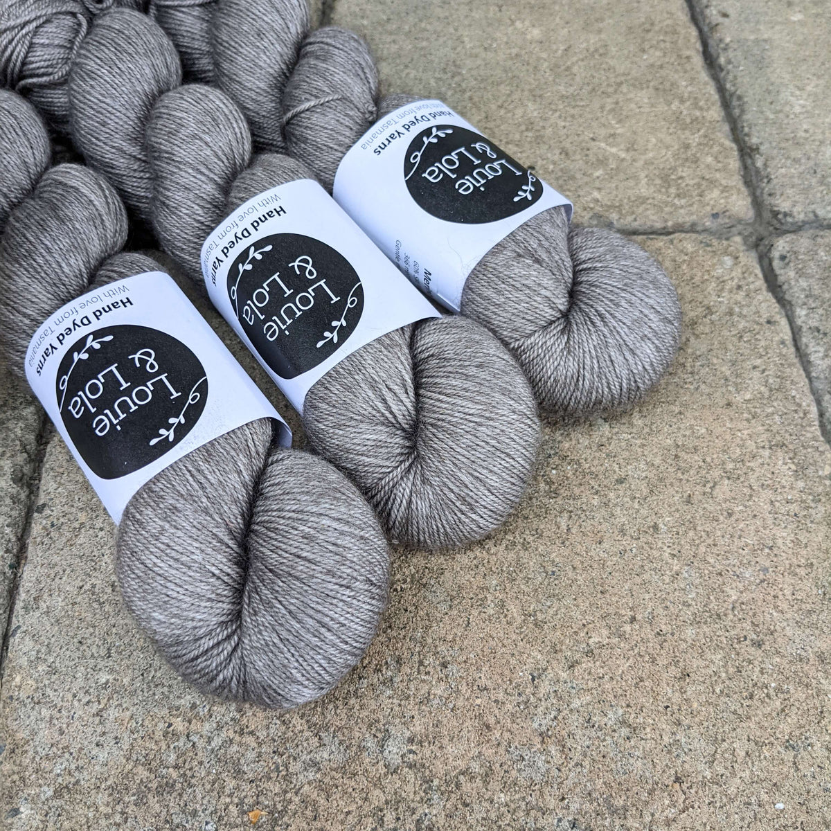 Gray skeins of yarn on a stone surface with labels from Walk Collection.