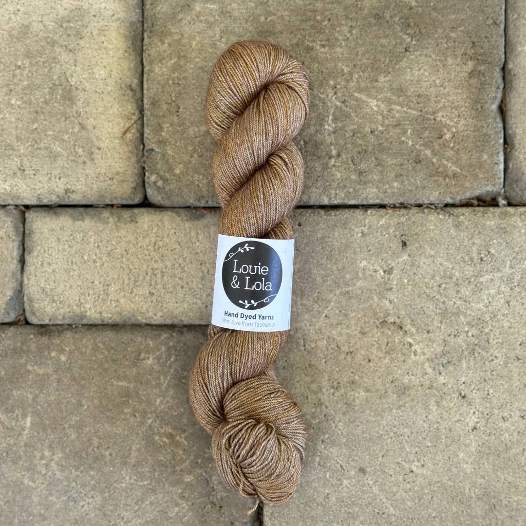 A skein of light brown yarn with a label on a textured stone background