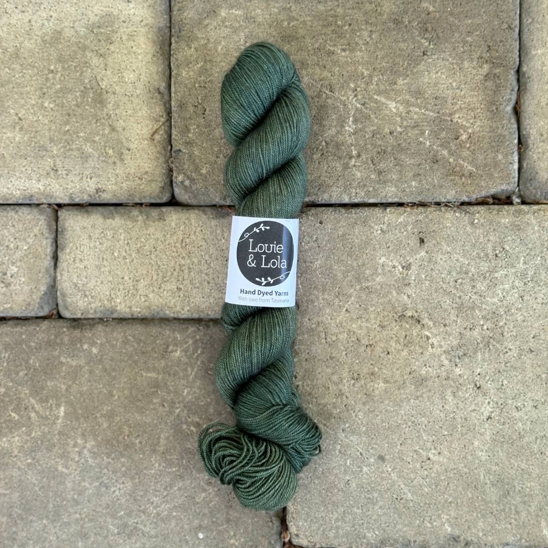 Green skein of hand-dyed yarn from Louie & Lola on stone background
