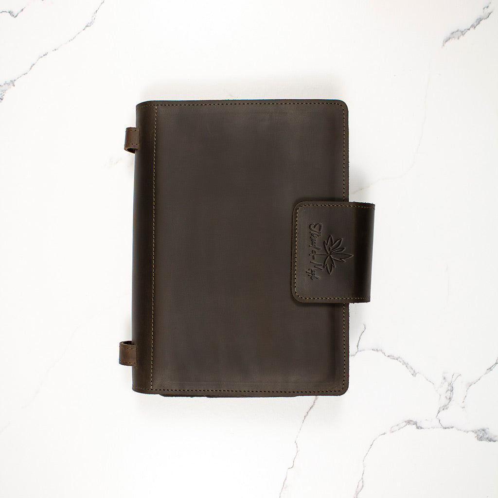Dark brown leather binder with logo on clasp, placed on a white marble surface.