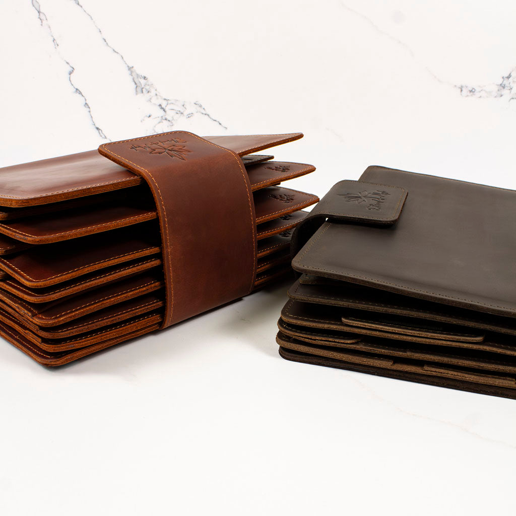 Stacked brown leather wallets with clasp and strap designs on a white marble surface.