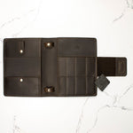 Open black leather wallet with multiple card slots, pockets, and a flap on a marble surface.